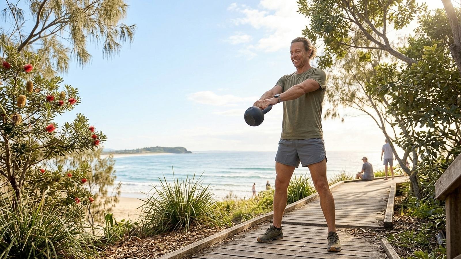 A man swings a kettlebell on a sunny beachside path.